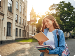 A young woman stands outside a university building, smiling as she reads from a notebook. With textbooks in tow and her blue shirt peeking from beneath a hefty backpack, she embodies the promise of new beginnings. The sunset casts a warm glow, capturing a moment worth storing in memory.